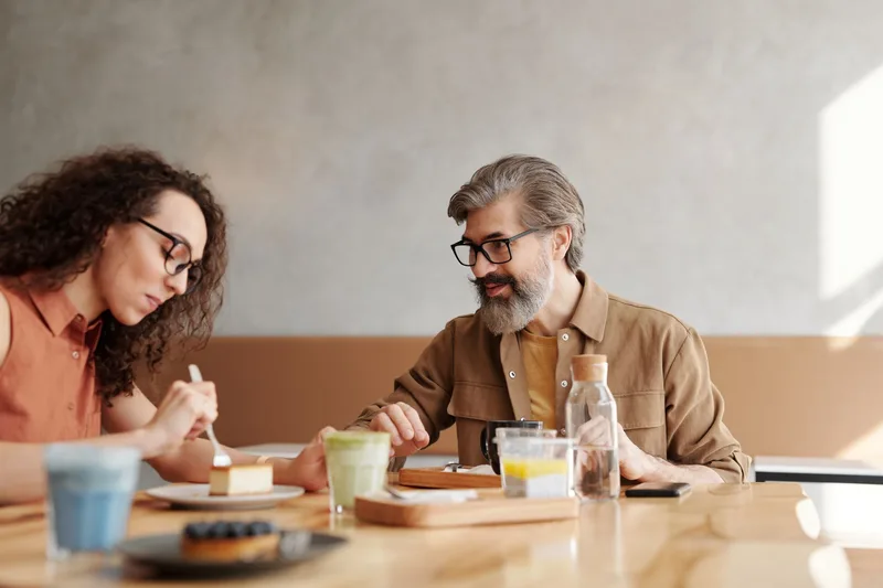 Two people talking at a café table, one of them writing notes as the other speaks