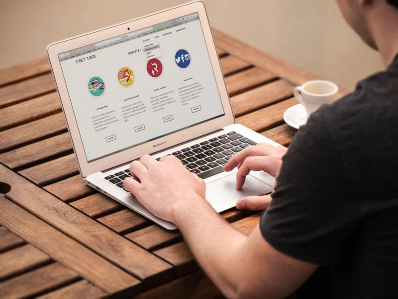 Person typing on a laptop at a table with a cup of coffee