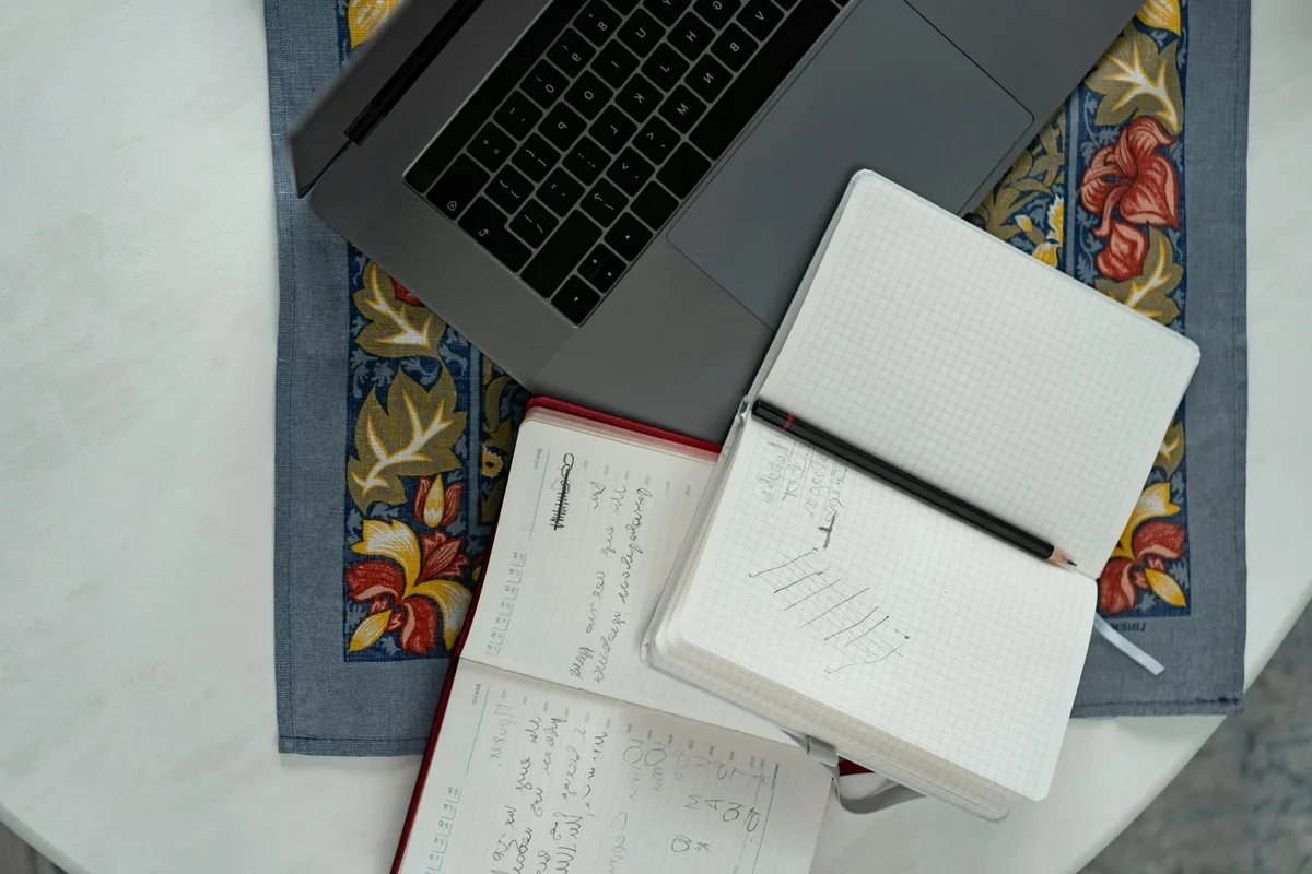 A solopreneur at a desk with a notebook and laptop, thinking through a product idea before committing to build it