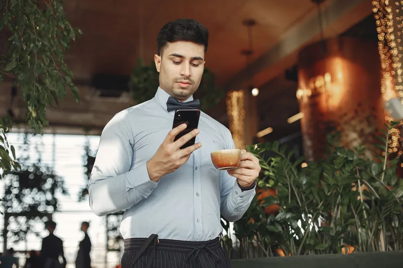 A person pausing to check their phone while holding a cup of coffee, the kind of quick moment where community threads, reviews, and search results get read